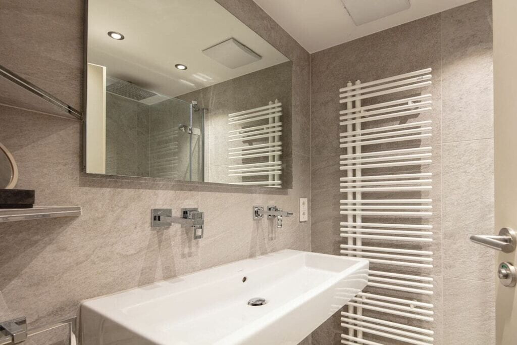 A modern bathroom with a large mirror, a white sink, and a glass-enclosed shower.