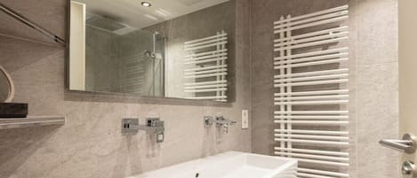 A modern bathroom with a large mirror, a white sink, and a glass-enclosed shower.