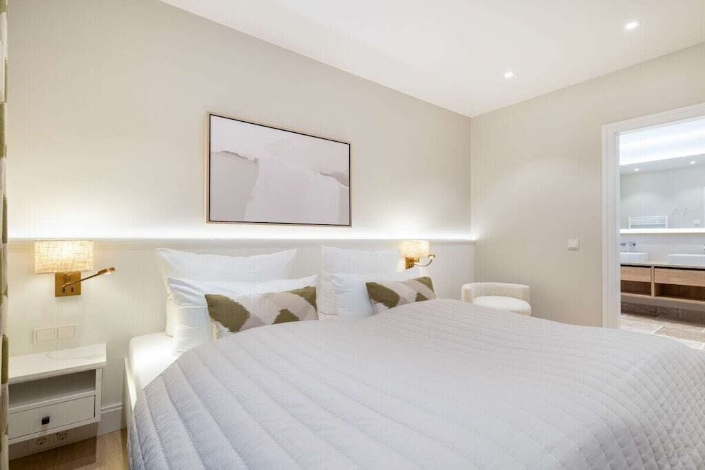 Habitación de hotel con una cama grande, mesitas de noche, una lámpara fijada a la pared y un baño visible a través de una puerta abierta.