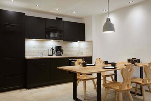 Una cocina moderna con muebles oscuros, una mesa de comedor de madera y una lámpara colgante.