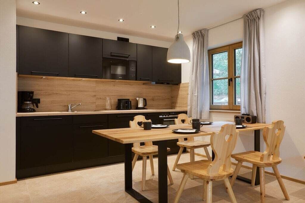 Une cuisine moderne avec des meubles de couleur sombre, un plan de travail en bois et un coin repas comprenant une table et des chaises.