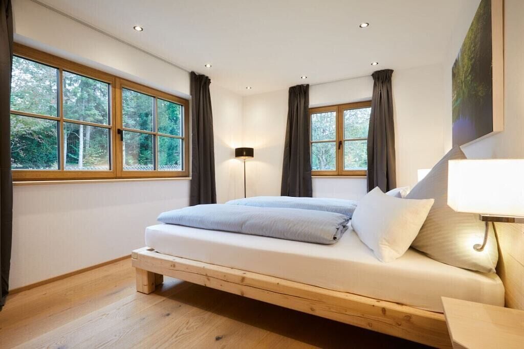 A bedroom with a wooden bed, large windows, and a floor lamp.