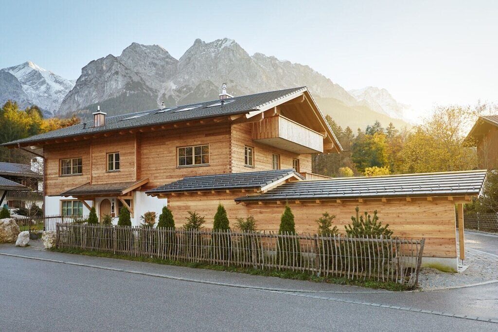 Une maison en bois à deux étages, dotée d’un balcon, qui se dresse sur un fond de paysage montagneux.