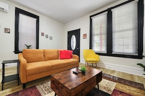Ein Wohnzimmer mit einer Couch, einem gelben Sessel, einem Couchtisch und einer Tür mit Glasfenster.