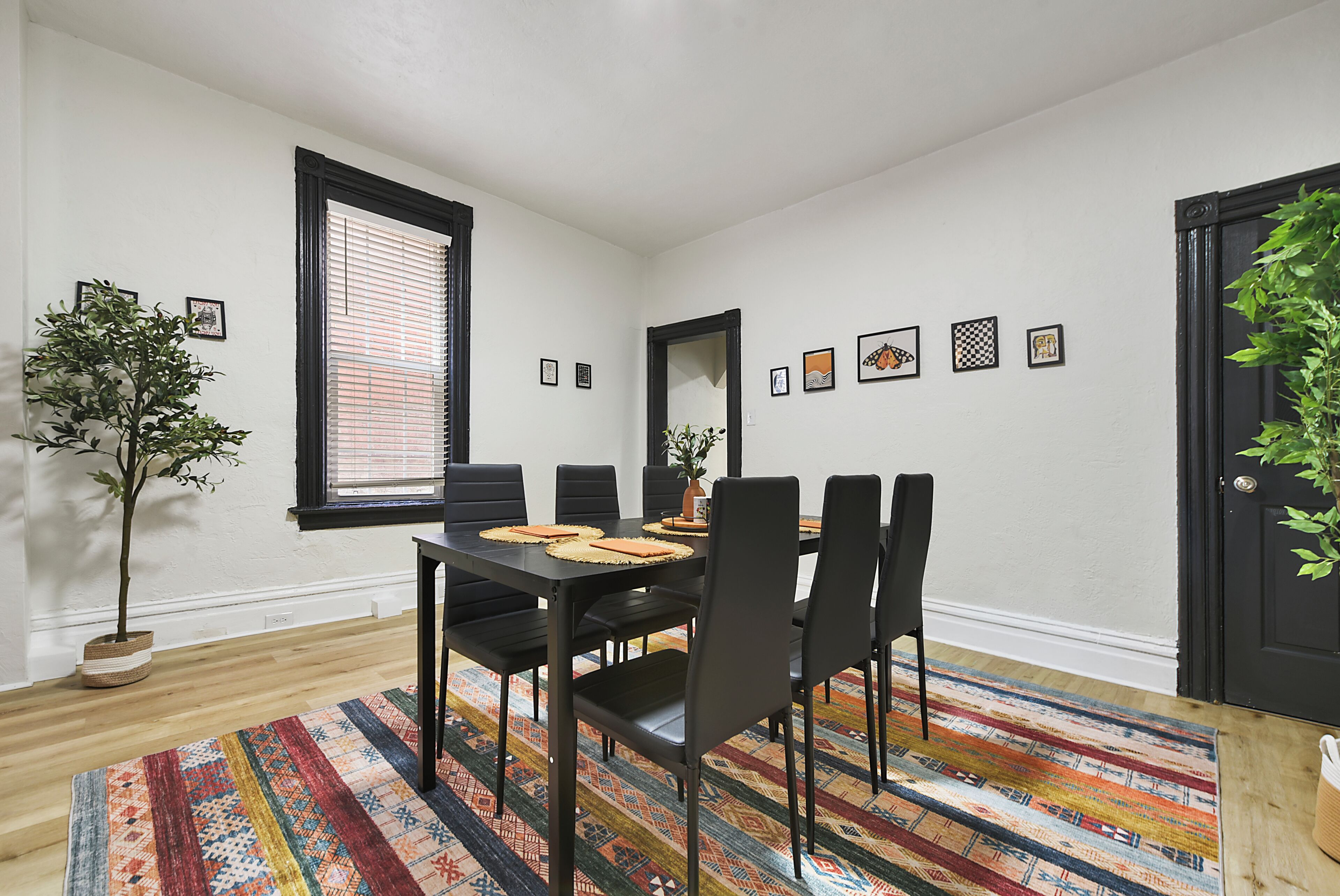 A dining area with a black table, chairs, and a colorful rug.