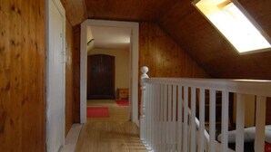 Interior em madeira com teto inclinado, corrimão branco e claraboia.