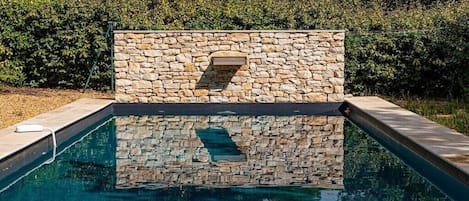 A swimming pool with stone walls and a built-in bench.