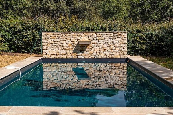 Une piscine avec des murs en pierre et un banc intégré.