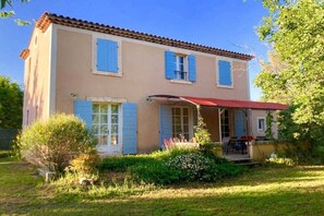 A two-story house with a red awning, a small porch, and a garden with various plants. - Charming country house with pool – 637 SAT (Saint Saturnin lès Apt)