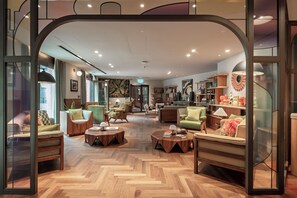 A modern hotel lobby with a herringbone wood floor, multiple seating areas, and a central coffee table. - Paddington Green by Veeve (London)
