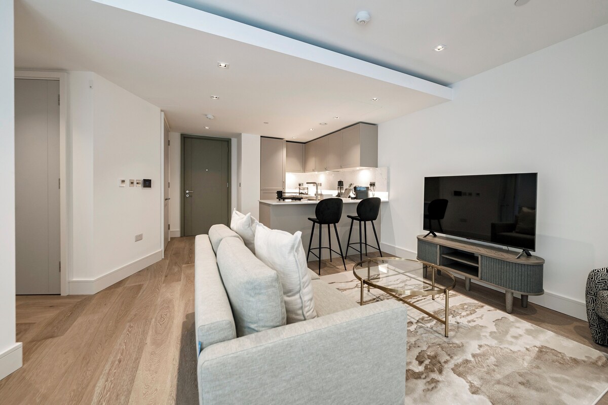Een moderne woonkamer met een grote flatscreen televisie, een bank en een eethoek met stoelen.