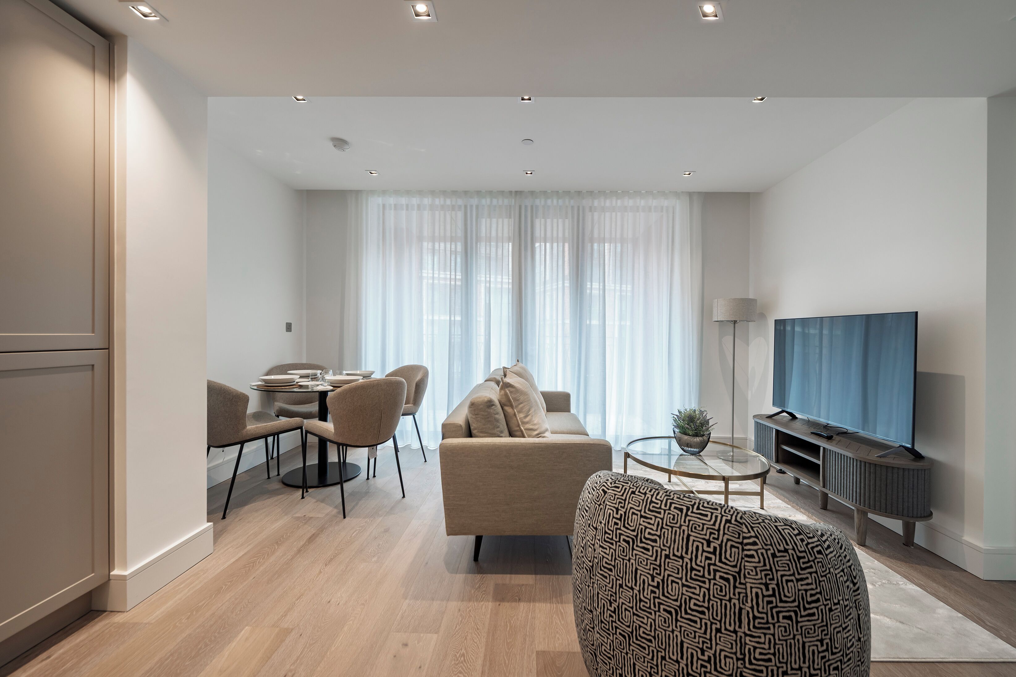 Een moderne woonkamer met een bank, een eettafel met stoelen, een televisie en een gestreept voetenbankje.