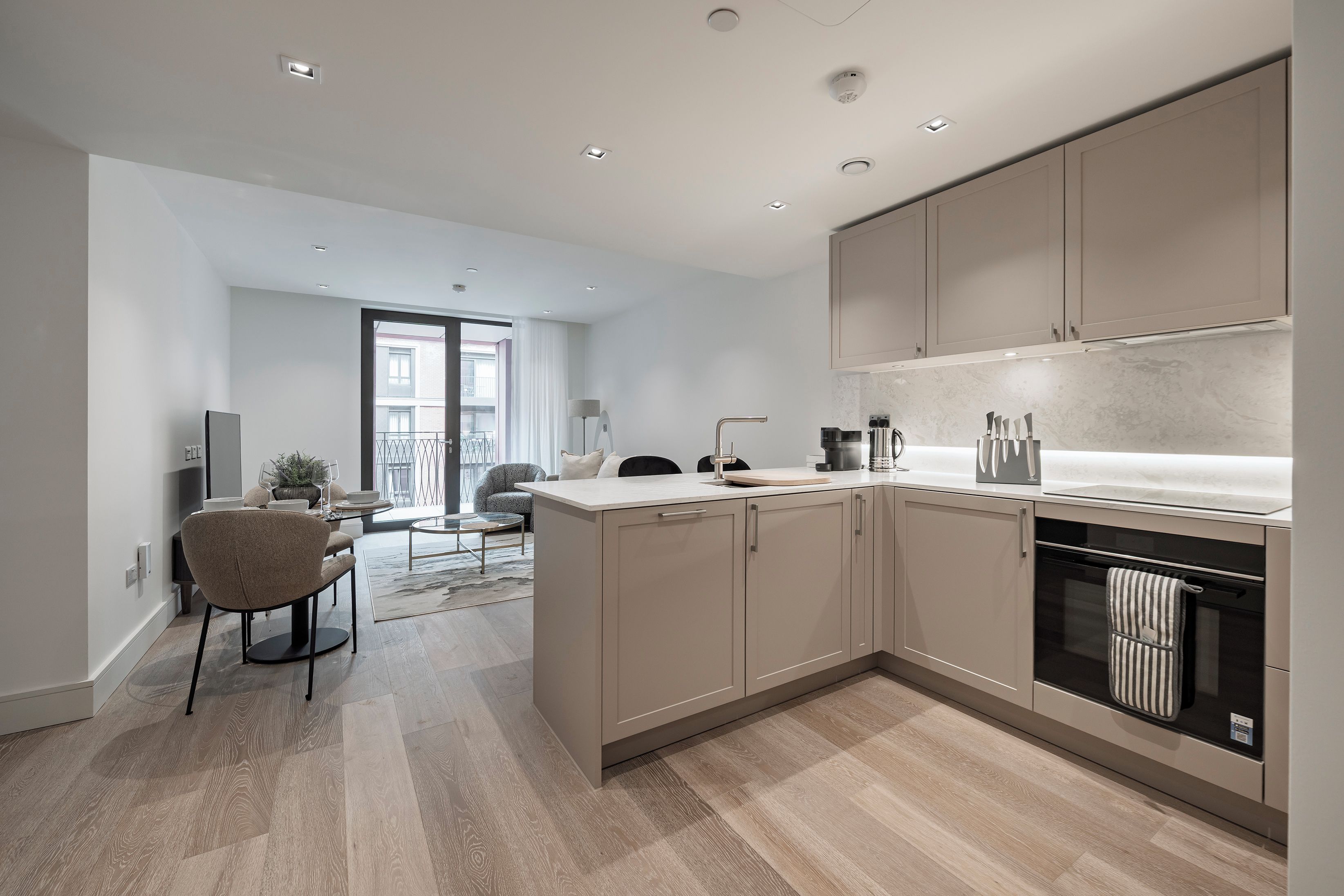 A modern kitchen with built-in appliances, a dining area with a round table and chairs, and a view of the outside balcony.