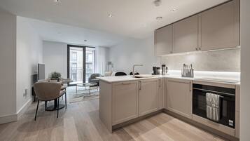 Una cocina moderna con electrodomésticos integrados, una zona de comedor con una mesa redonda y sillas, y vistas al balcón exterior.