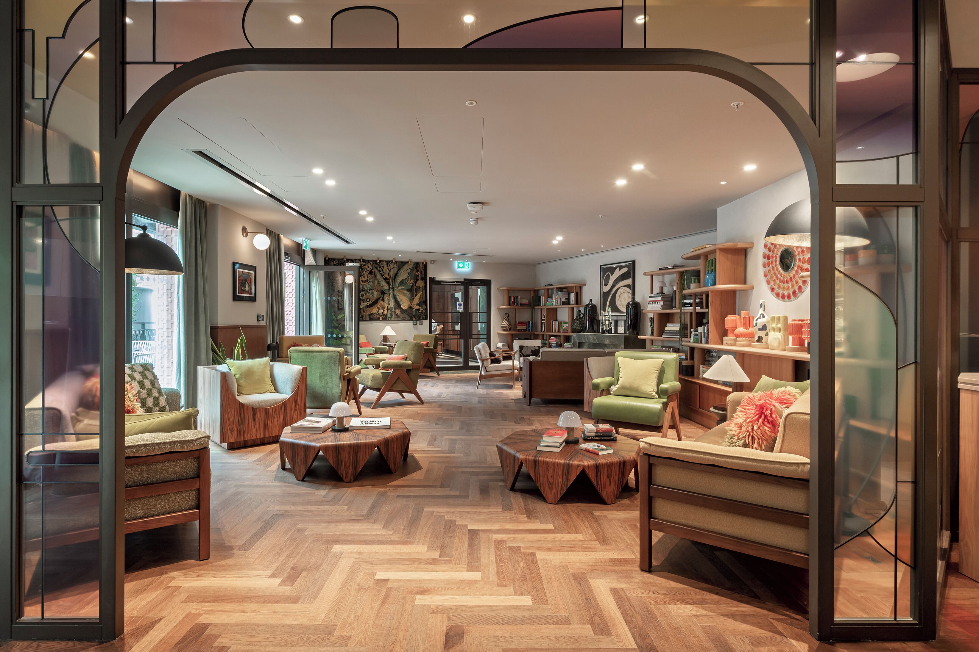 A modern hotel lobby with a herringbone wood floor, multiple seating areas, and a central coffee table.