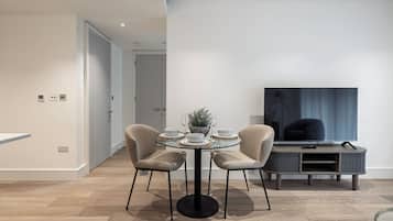 Una sala moderna con una mesa de comedor para dos personas, un televisor y un sofá.