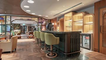 Un espace bar moderne comprenant un comptoir, des tabourets et un réfrigérateur rempli de boissons.