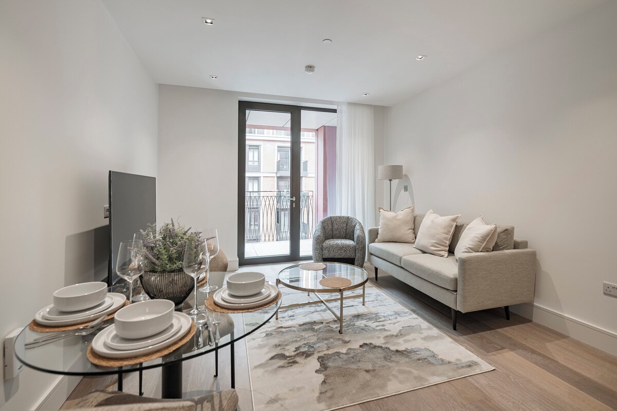 Een moderne woonkamer met een bank, een glazen salontafel en een eethoek met borden en glazen.