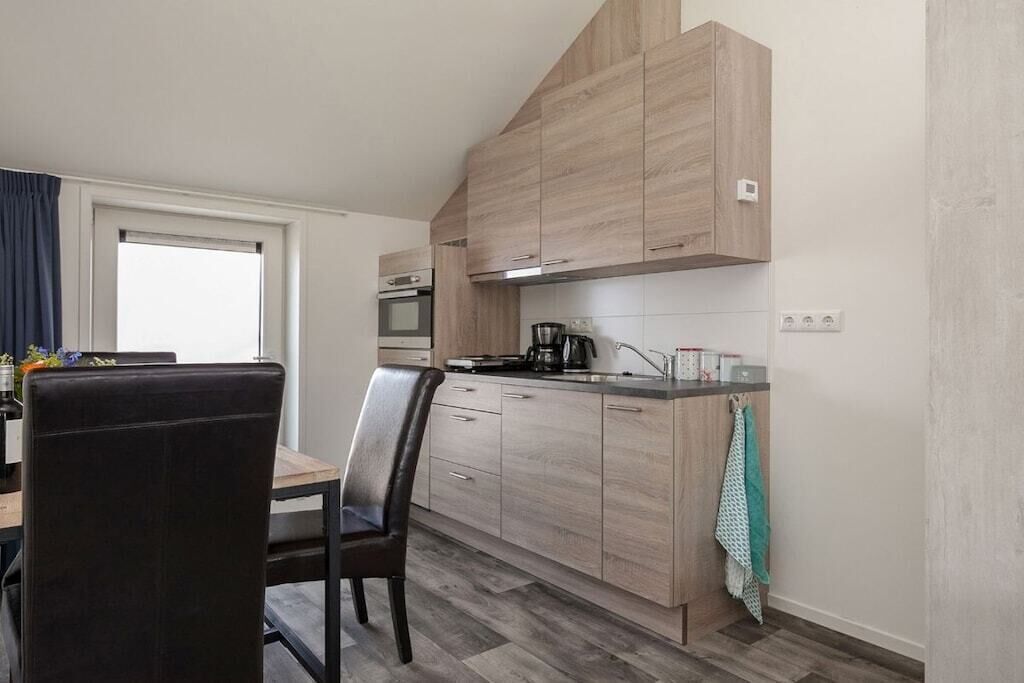 Een moderne keuken met houten kastjes, een eettafel met stoelen en een raam met gordijnen.