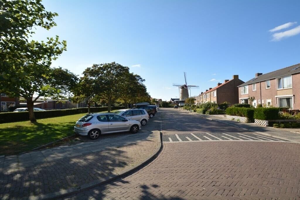 Una strada residenziale con auto parcheggiate, un mulino a vento sullo sfondo e case con facciate in mattoni.