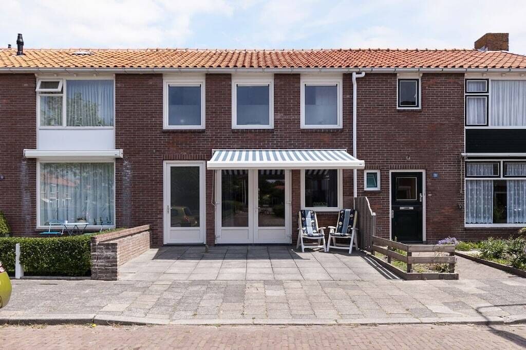 Un edificio residencial de dos pisos con fachada de ladrillo, una puerta principal y un pequeño patio con mobiliario exterior.