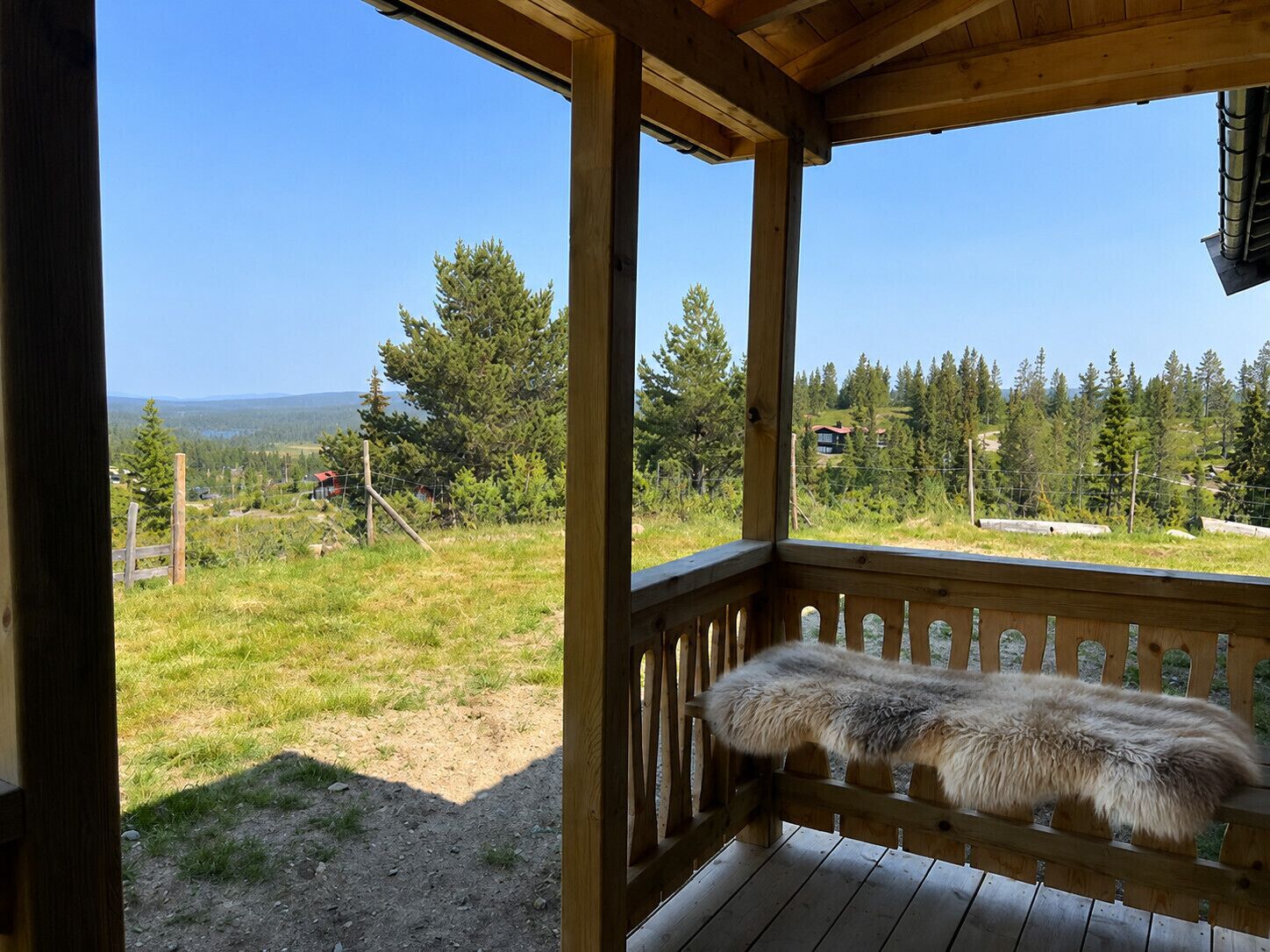 En træterrasse med et pelsunderlag, med udsigt over en græsplæne med træer og fjerne bjergkæder.