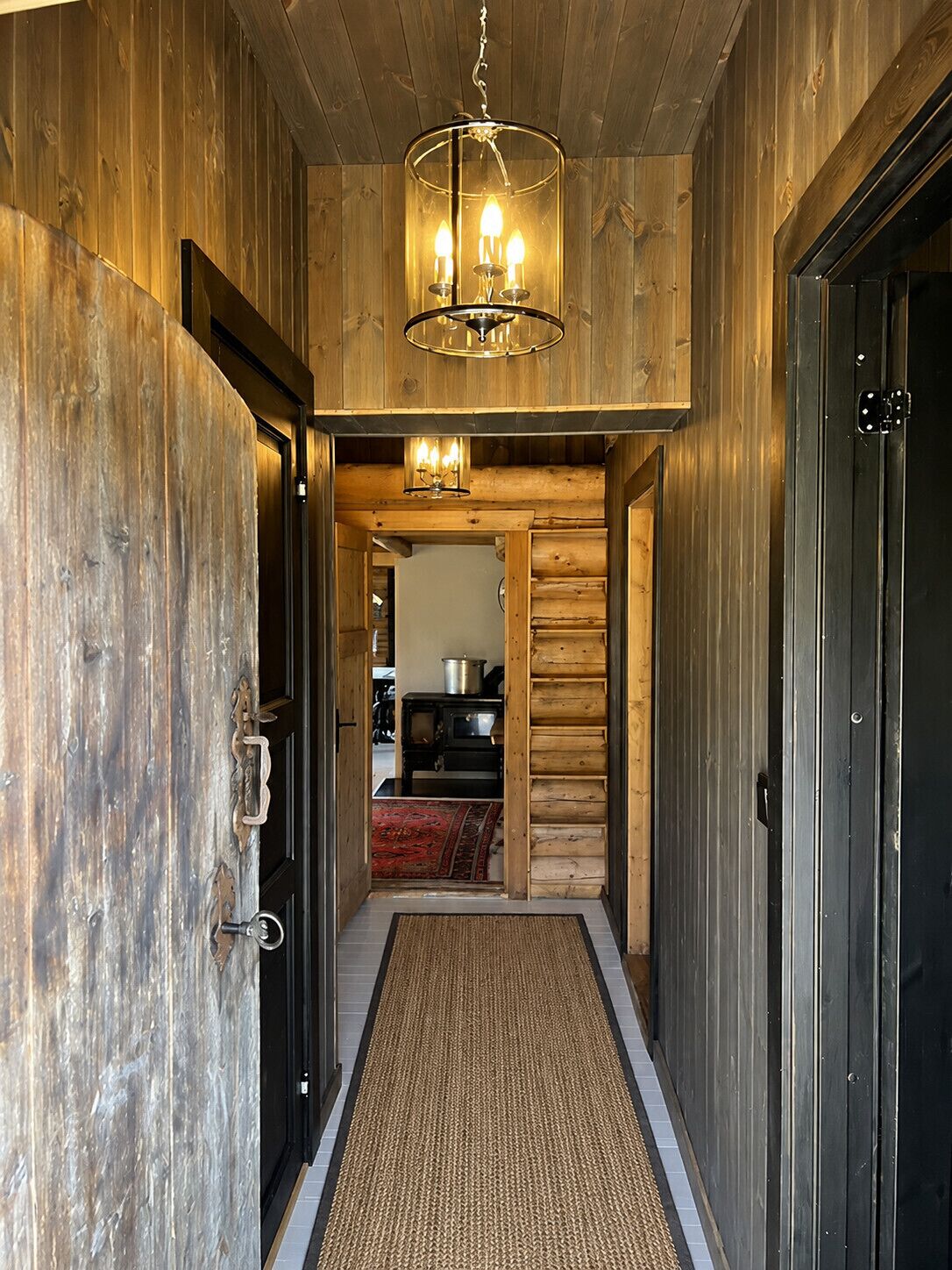 Pasillo interior de madera con candelabro, felpudo y cocina visible a través de una puerta abierta.