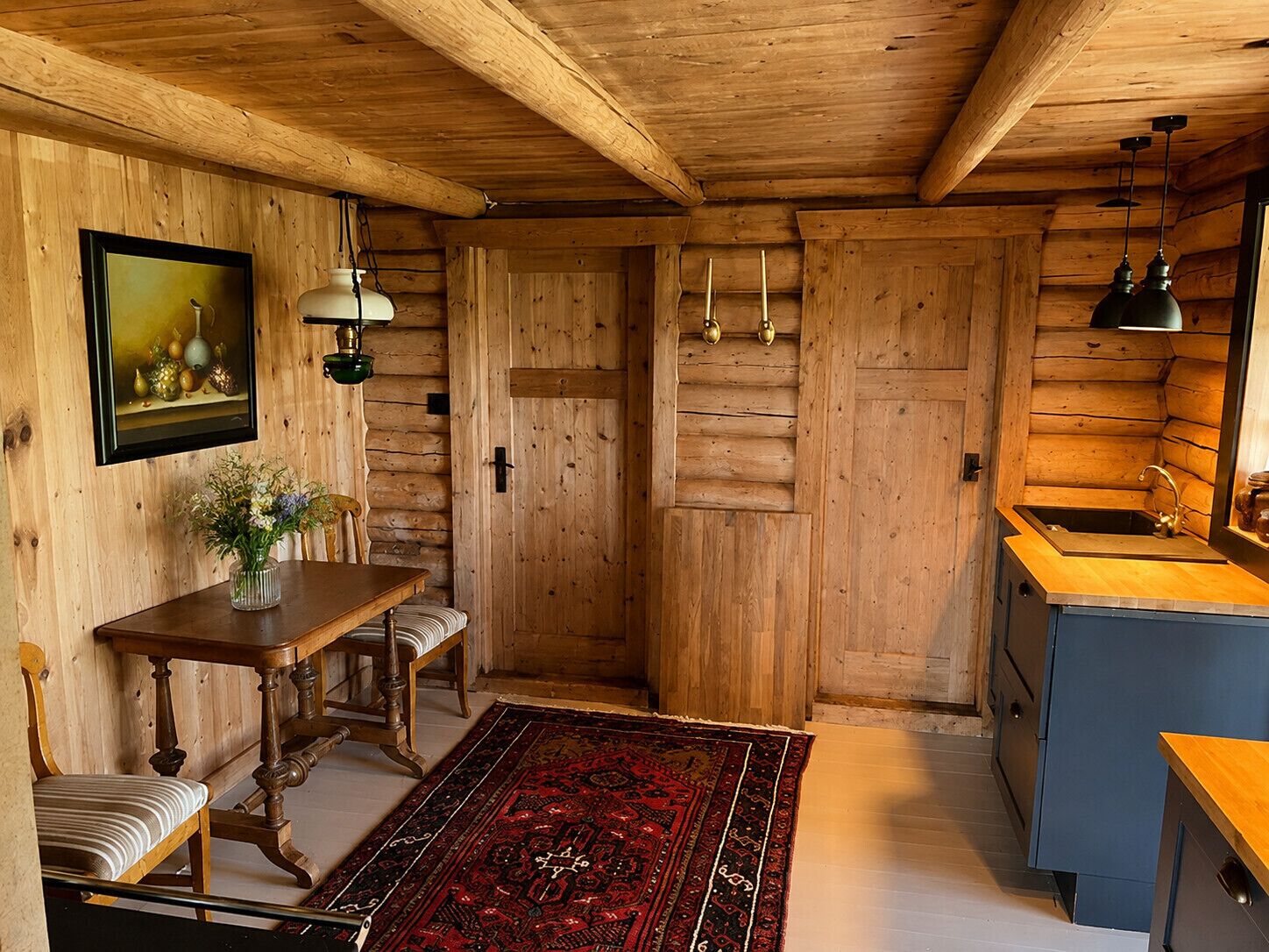 A wooden interior with a dining table, bench, and a rug.