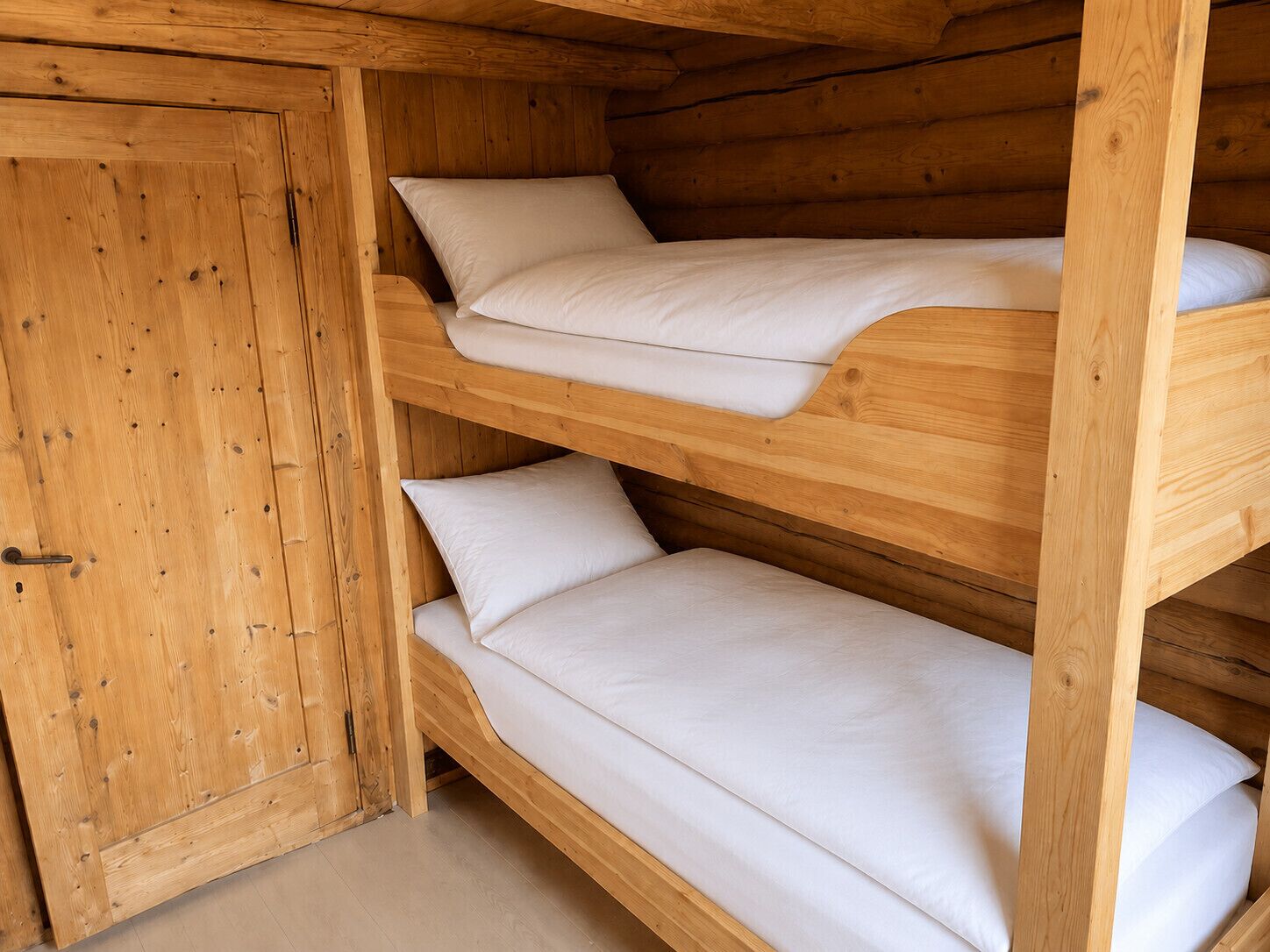 Una cama litera de madera con dos niveles, cada uno con colchón y almohadas.