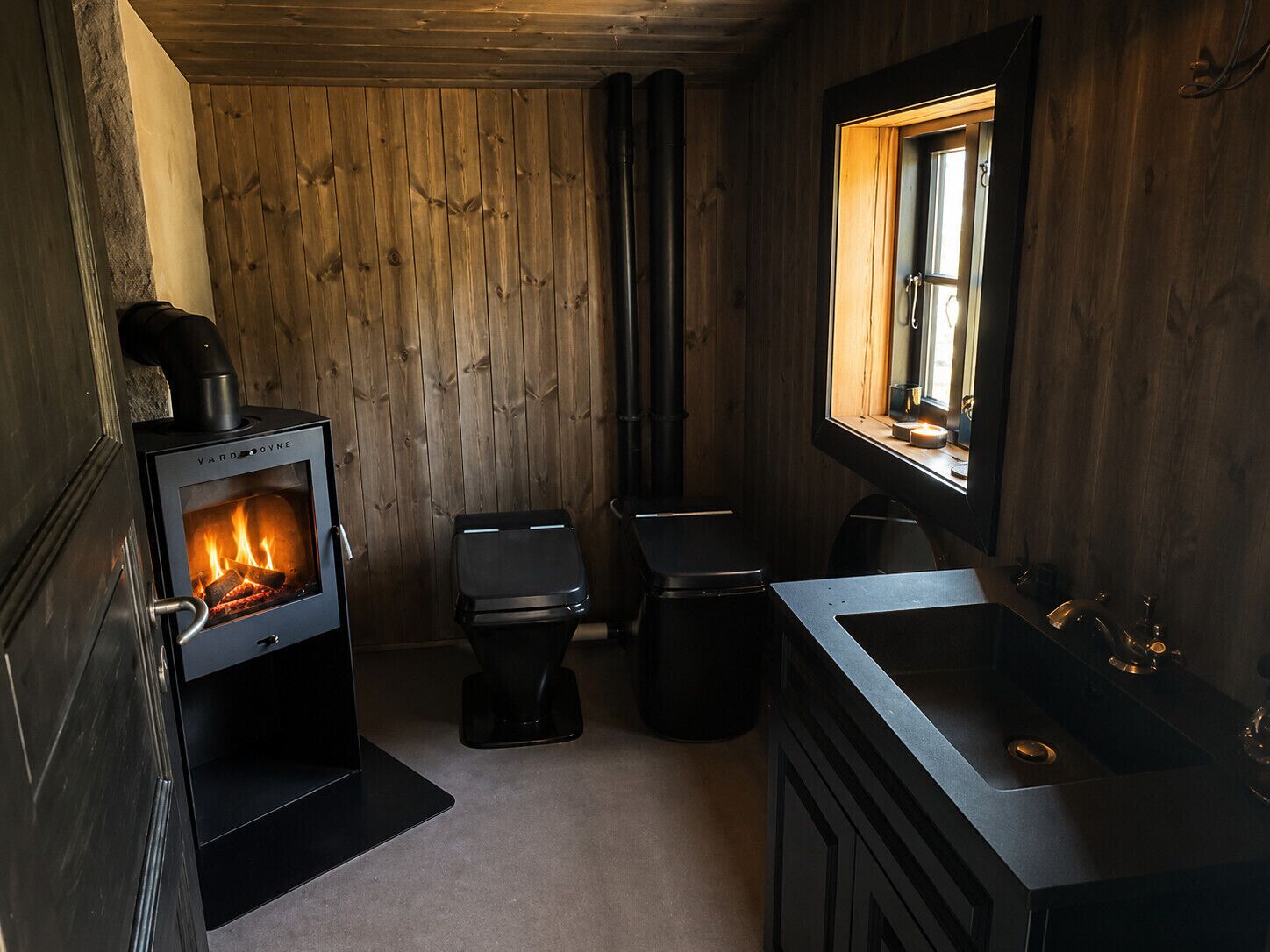 Une petite salle de bain équipée d’un poêle à bois, de deux toilettes et d’un lavabo.
