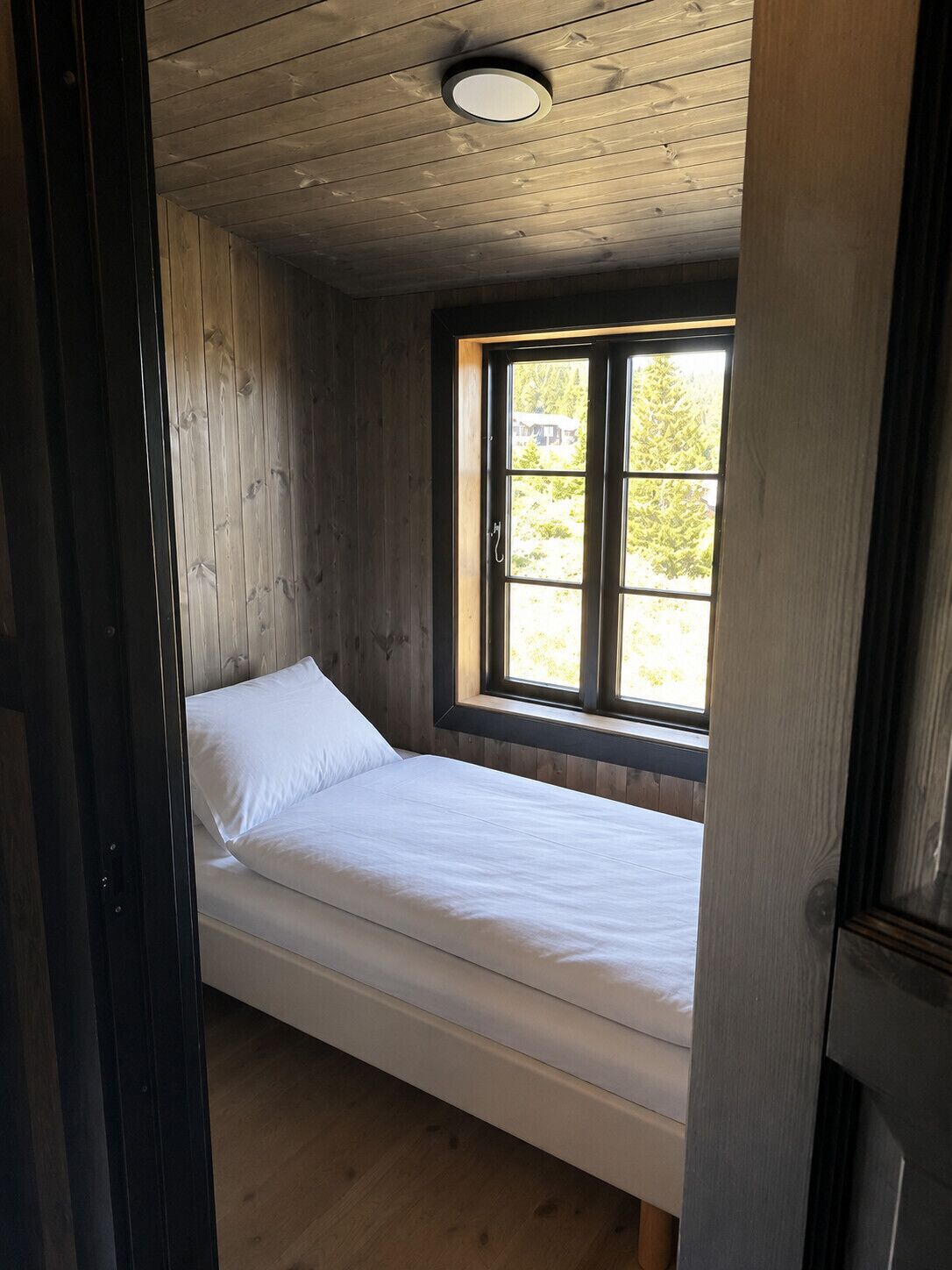 Un lit simple dans une pièce aux murs en bois et dotée d’une fenêtre.