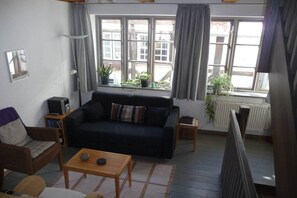 Ein Wohnzimmer mit einer Couch, einem Couchtisch, einer Lampe und Blick ins Freie durch große Fenster.