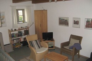 A living room with a television, two wicker chairs, a bookshelf, and a window with curtains. - Holiday apartment with 1 bedroom (Lübeck)