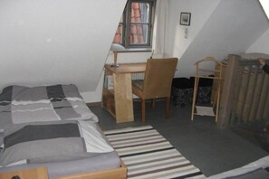 A small, compact room with a bed, a desk, and a chair. There is a window with a view of a building outside. - Holiday apartment with 1 bedroom (Lübeck)