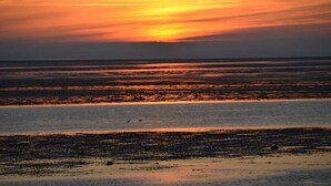 A sunset over a beach with calm waters reflecting the sky. - Holiday home in Alkersum with swimming pool (Alkersum)
