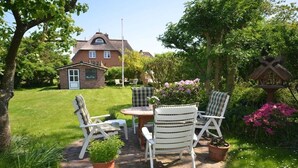 A patio with a table and chairs, surrounded by potted plants and a house in the background. - Holiday home in Alkersum with swimming pool (Alkersum)