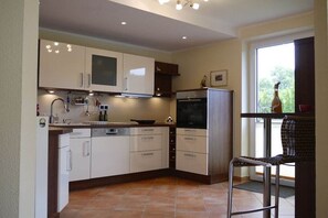 A compact kitchen with white cabinets, a built-in oven, and a dining area with a chair. - Holiday apartment with 2 bedrooms (Bad Zwischenahn)