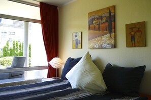 A hotel room with a bed, a window with red curtains, and artwork on the wall. - Holiday apartment with 2 bedrooms (Bad Zwischenahn)
