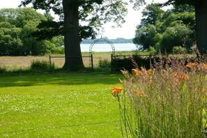 A grassy area with a metal gate, trees, and a body of water in the background. - Holiday apartment with 2 bedrooms (Bad Zwischenahn)