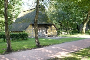 A traditional building with a thatched roof, surrounded by trees and a paved walkway. - Holiday apartment with 2 bedrooms (Bad Zwischenahn)