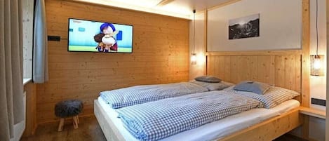 A wooden-paneled room with a bed, a television mounted on the wall, and a small stool.