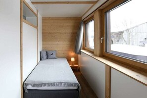 Ett litet rum med en säng, ett fönster och ett nattduksbord med en lampa.