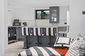 A compact kitchen with a bar stool area, a microwave, an oven, and a window with a plant. - Large 5BR Home in Newport | Ideal for Work Crews | Sleeps 12 (Newport)