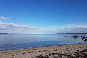 Een strand met rustig water, een zandkust en veraf gelegen landschappen.