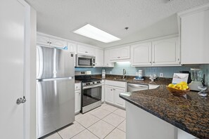 A modern kitchen with stainless steel appliances, white cabinetry, and a granite countertop. - Phoenix V 504 by Liquid Life (Orange Beach)