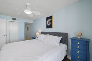Ein Schlafzimmer mit einem Bett, einem Nachttisch, einer Kommode, einem Deckenventilator und einem Bilderrahmen mit einer Meeresschnecke an der Wand.