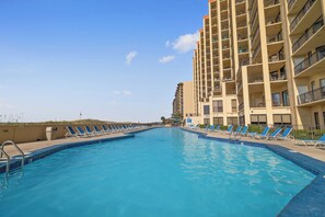 A swimming pool with blue water, surrounded by lounge chairs and a tall building with balconies. - Phoenix V 504 by Liquid Life (Orange Beach)