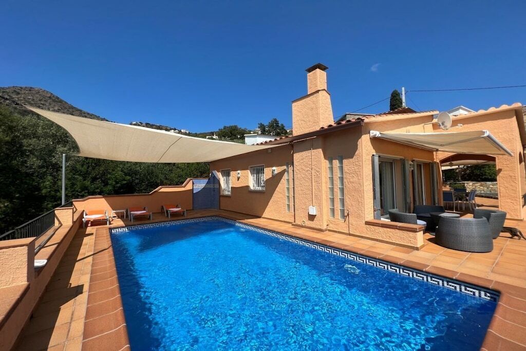 A swimming pool with a sunshade, outdoor furniture, and a mountain backdrop.