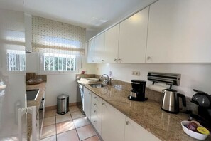 A kitchen with white cabinets, a granite countertop, a stainless steel sink, a coffee maker, and a kettle. - Holiday home in Roses with swimming pool (Roses)