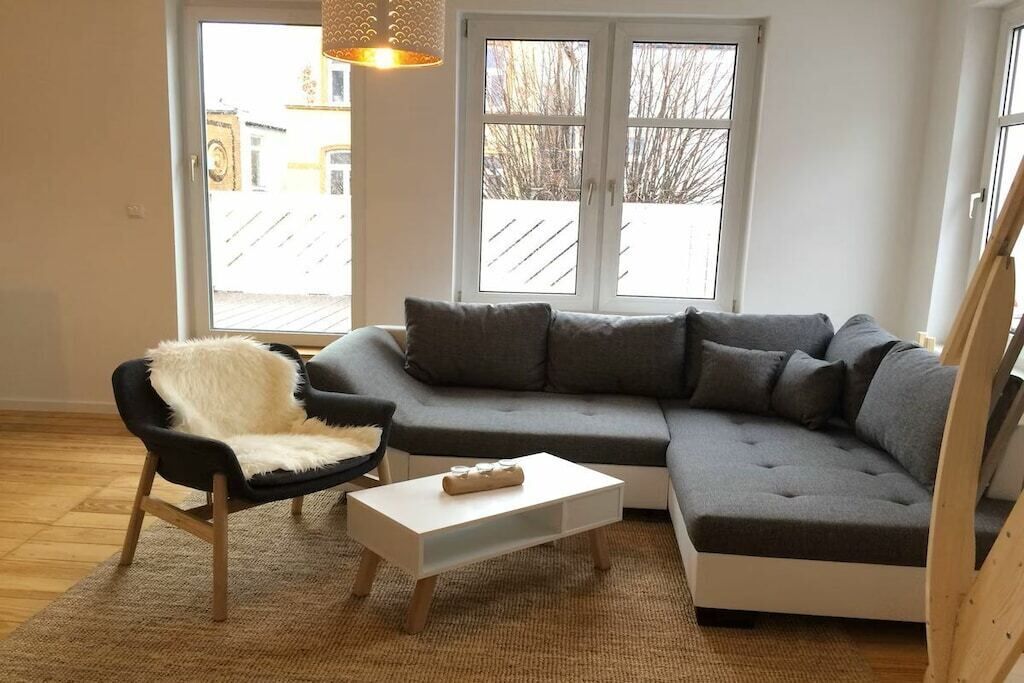 Ein modernes Wohnzimmer mit einem grauen Ecksofa, einem weißen Couchtisch und einem schwarzen Sessel mit weißer Decke.